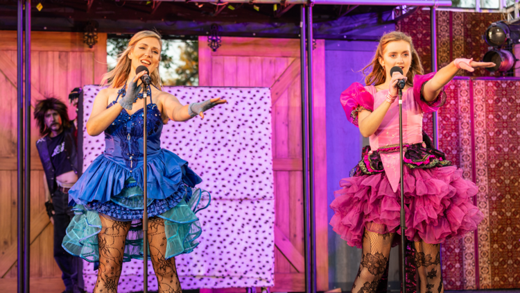 Two actors wearing glam rock style costumes sing on-stage in Much Ado About Nothing
