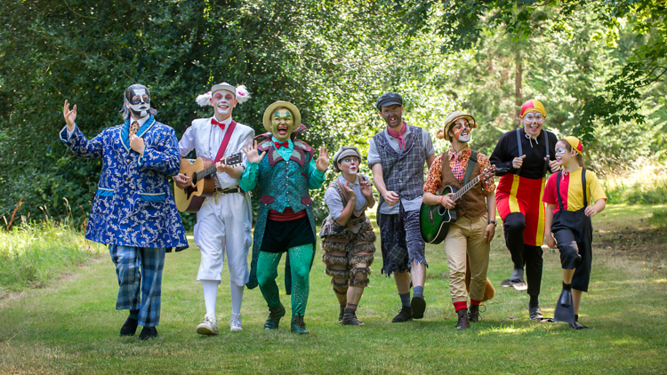 The cast of Wind in the Willows walks in a line on some grass with jovial expressions