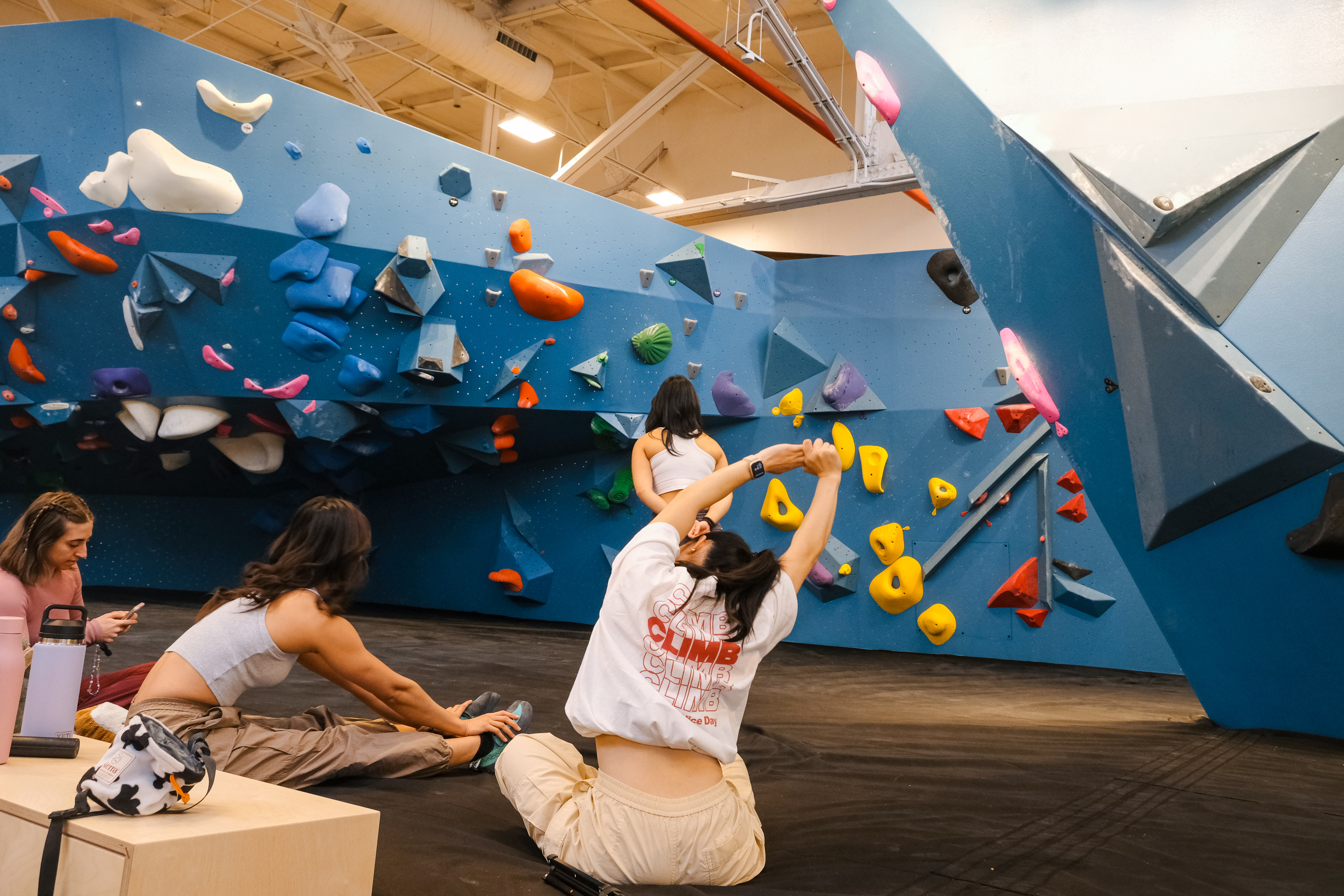A woman stretches in front of a climbing wall.