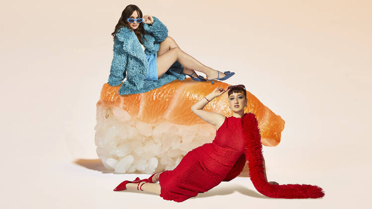 Two women posing next to a giant piece of sushi