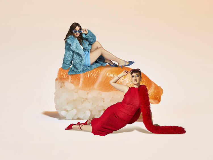 Two women posing next to a giant piece of sushi