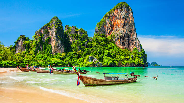 Boats lined up at a pristine, secluded beach in Krabi, Thailand.
