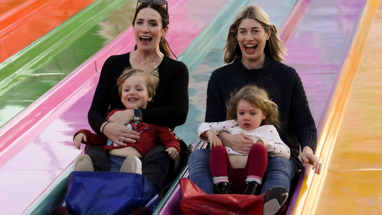 Two mums and their sons sliding down a rainbow slide