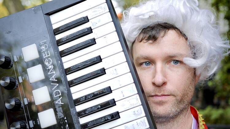 A man holding up a keyboard while wearing a white wig.