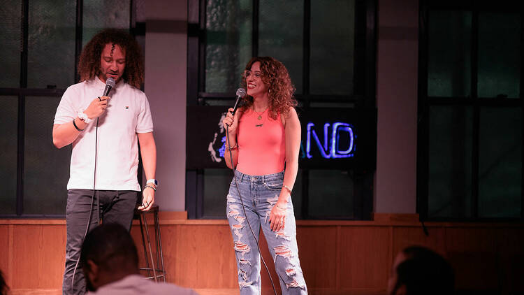 Two comedians stand on a stage holding microphones