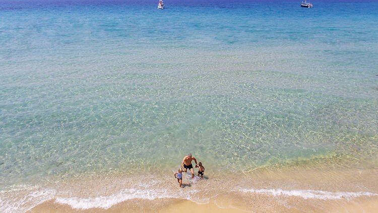 A man and two children play in the sea in the Sani Resort, Greece