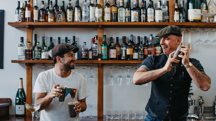 Two smiling bartenders mixing drinks behind the bar.
