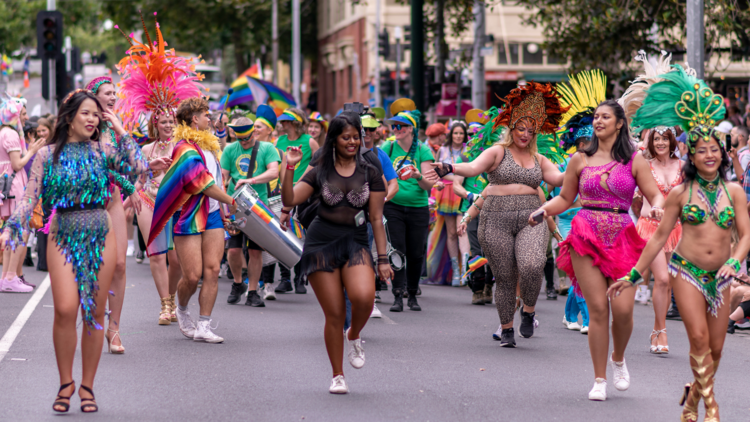 People in vibrant costumes with feather headpieces walk in the pride march