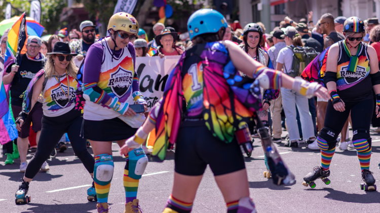 People on roller skates in the pride march, one wearing rainbow wings