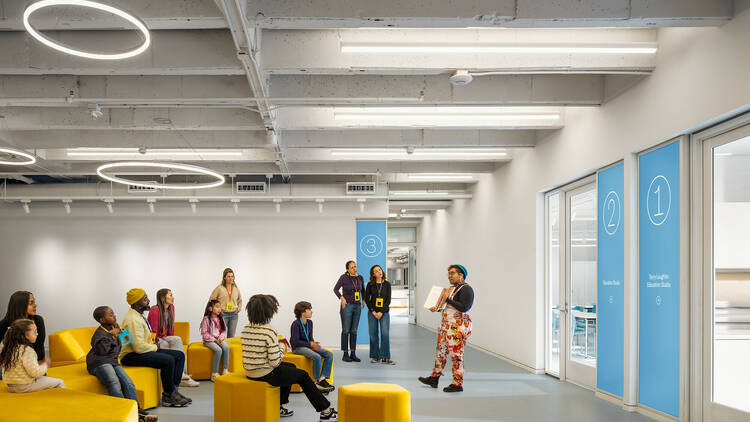 Kids and adults sit on yellow chairs at the museum's education space.