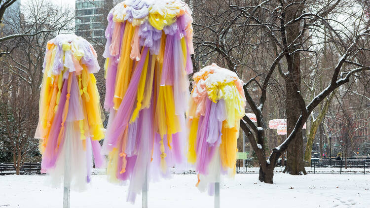 Three sculptures in a snowy Madison Square Park. The sculptures are made of yellow and lilac tulle.