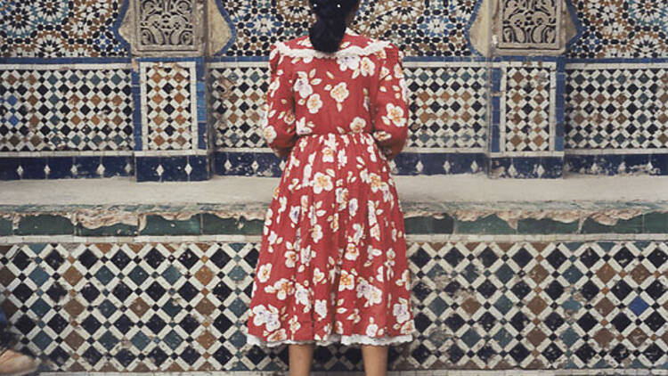 A woman in a red dress in front of a tile wall.