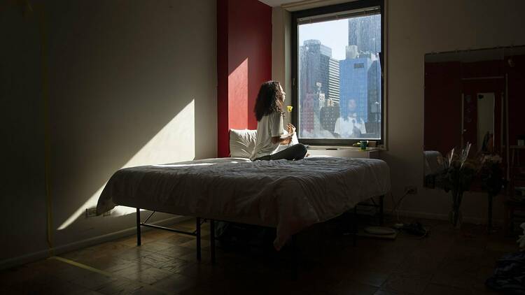 A person sits on a bed looking out at the nyc skyline.