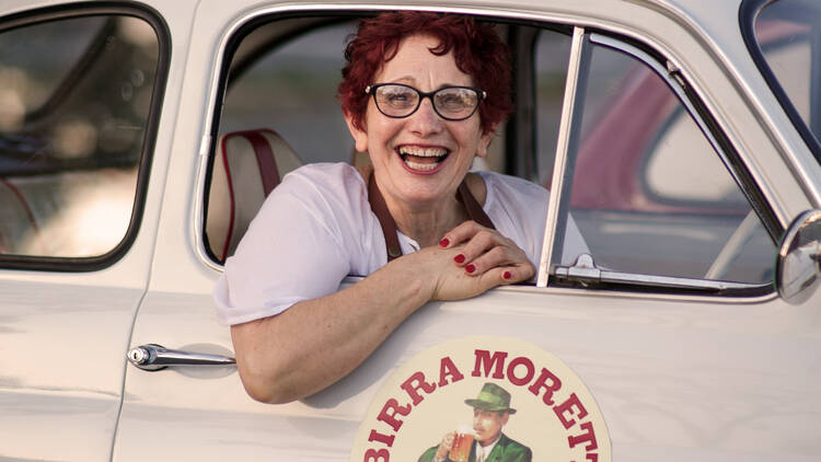 A smiling Italian grandmother in a Birra Moretti branded vehicle.