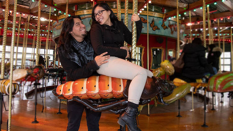 Two people ride a roach themed carousel
