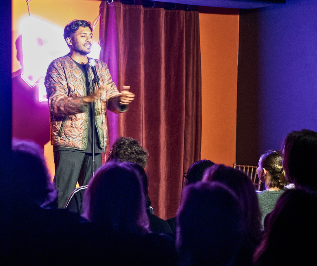 A performer on stage in front of a Flop House neon sign.