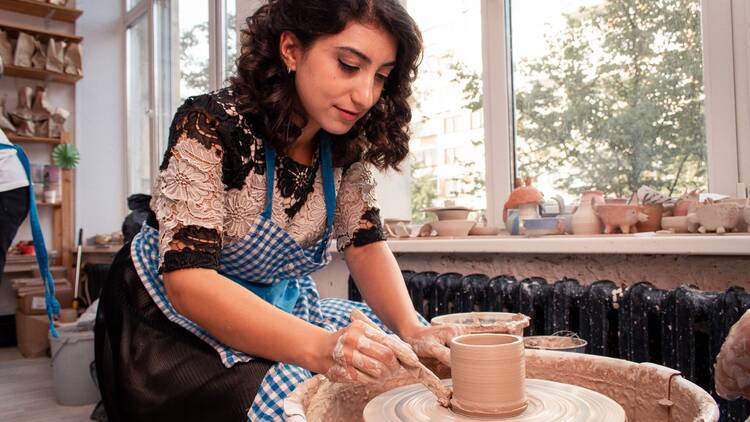 A woman makes pottery at a wheel.