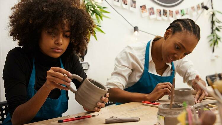 Two women work on making pottery.