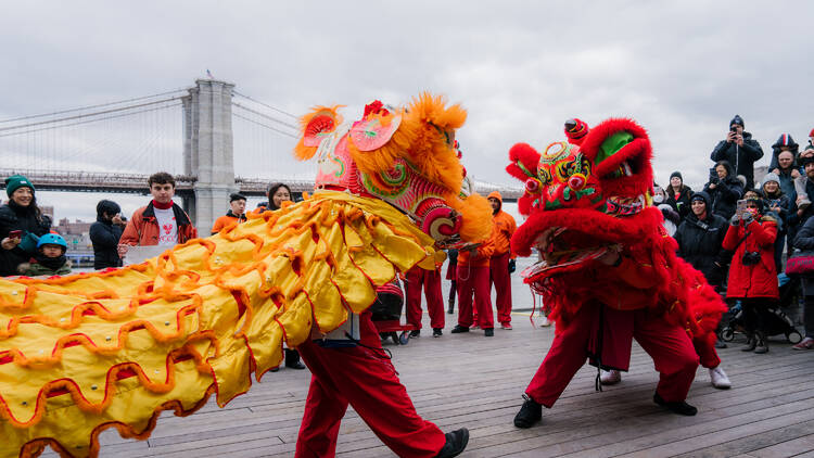 Two dragon dancers in front of the Brooklyn Bridge