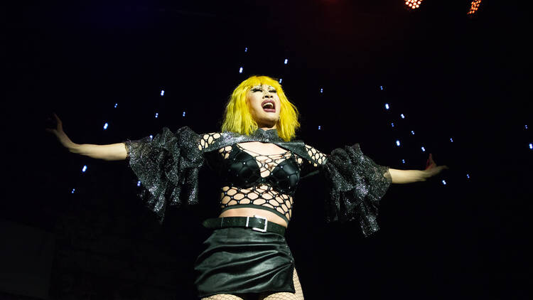A drag queen spreads her arms on a stage