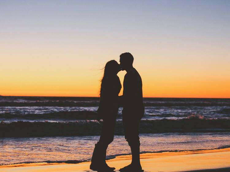 A couple kissing, silhouetted in front of the ocean at sunset. 