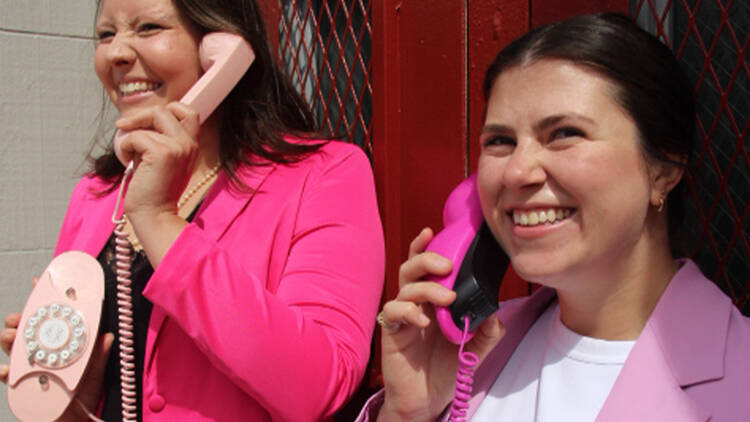 Two people dressed in pink hold wire phones up to their ears