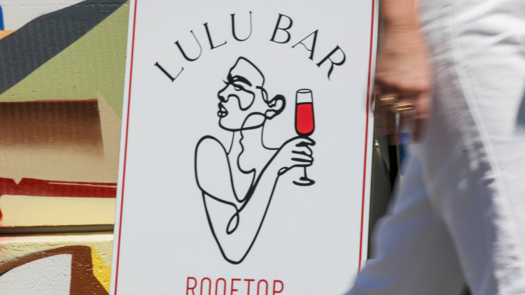 Person in white trousers walking past the Lulu Bar sign. 