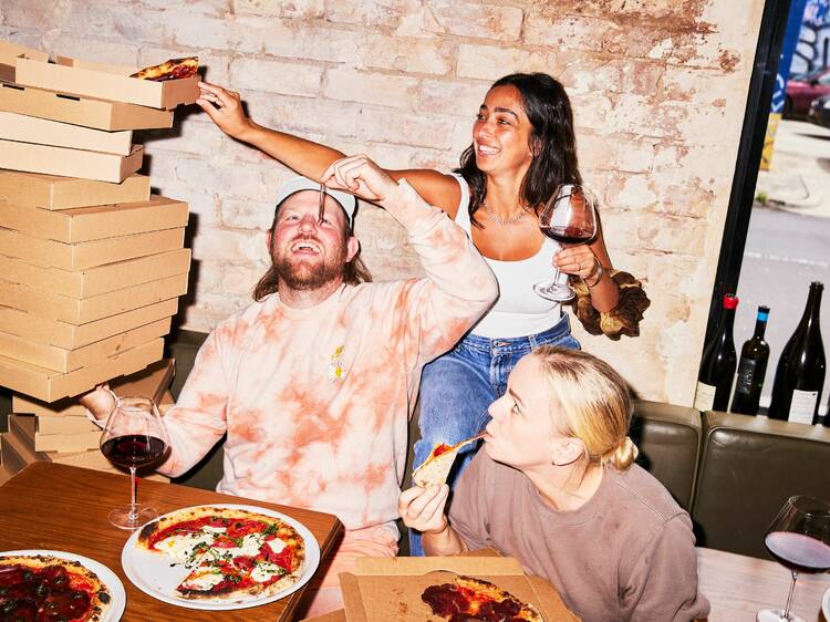 Group of friends smiling and tucking into boxes of pizzas.