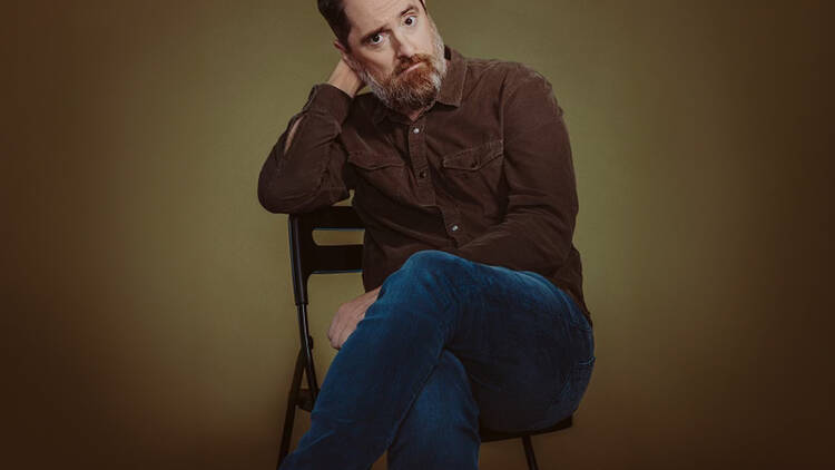 A man sits on a chair against a brown backdrop