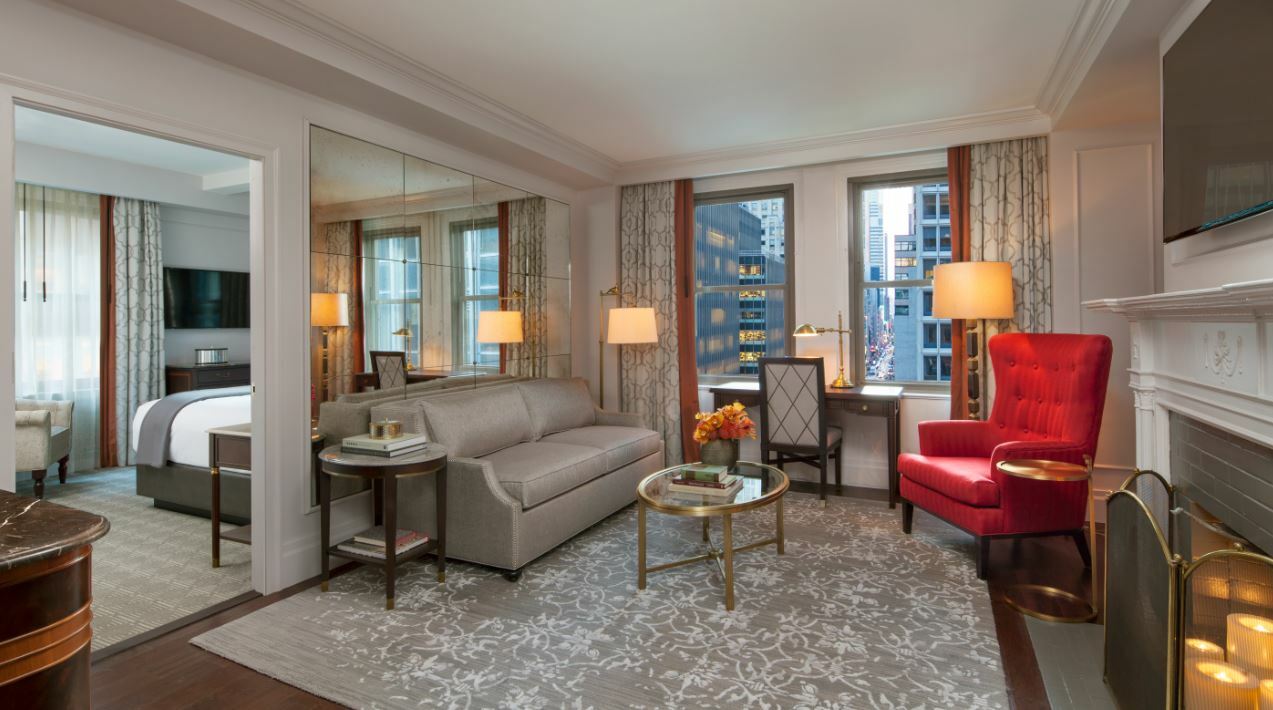 A hotel suite with a plush couch and red chair.