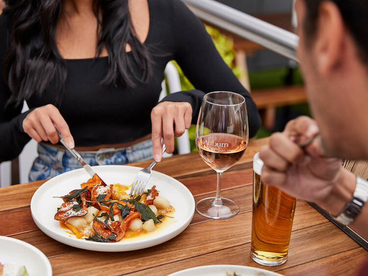 Pair of pub-goers enjoying a meal and a drink at a wooden bench in Auburn Hotel's beer garden.