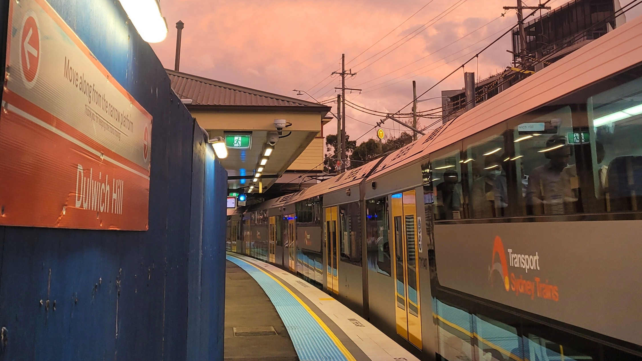 A train stopped at a station with a pretty pink sunset in the sky.