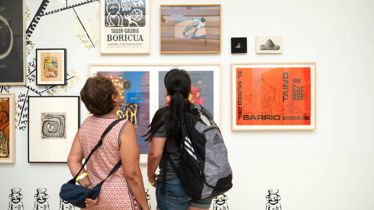 Two women look at artwork on a wall.