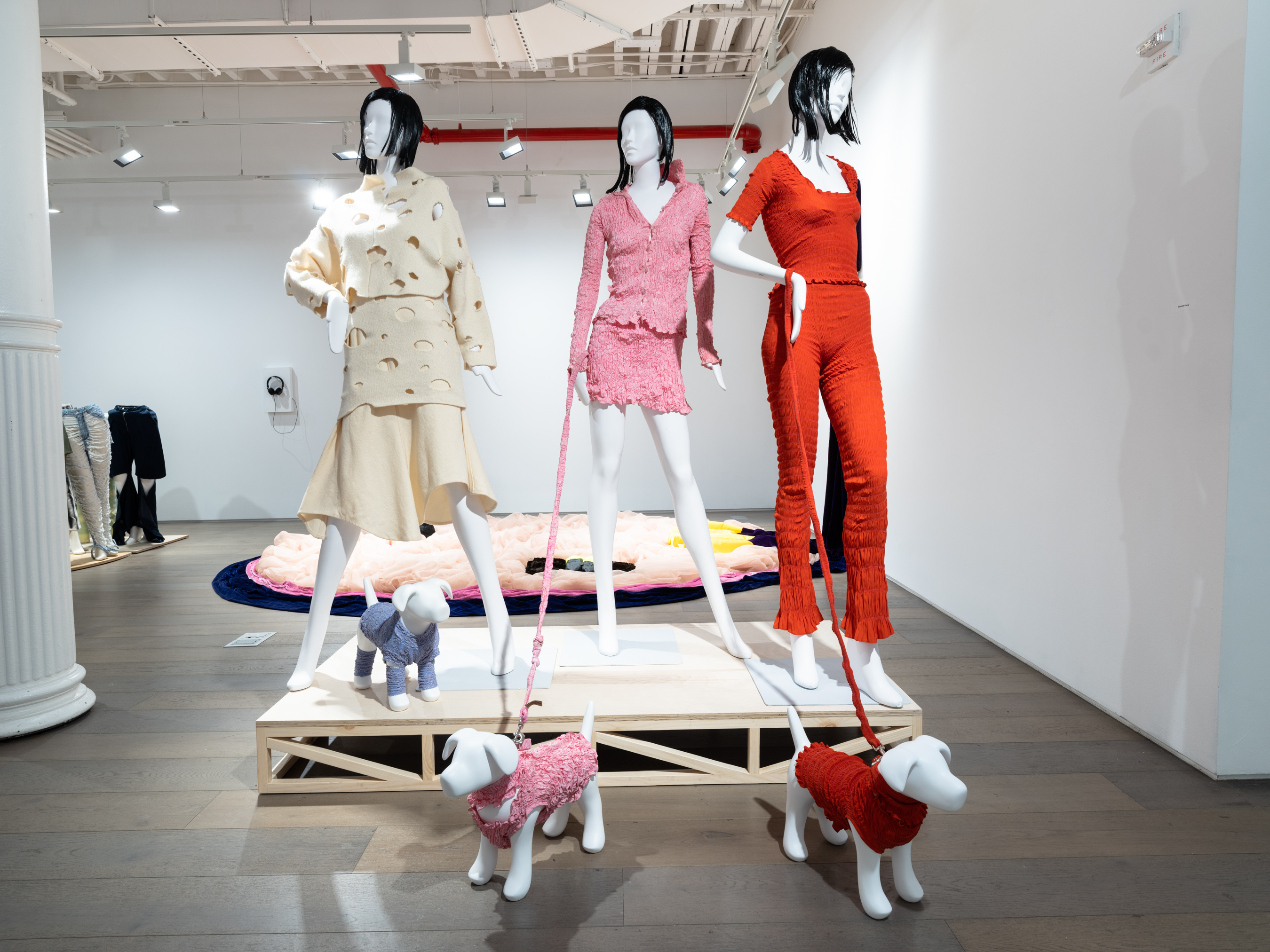 Mannequins dress in beige, pink, and red outfits with matching outfits for their dogs.