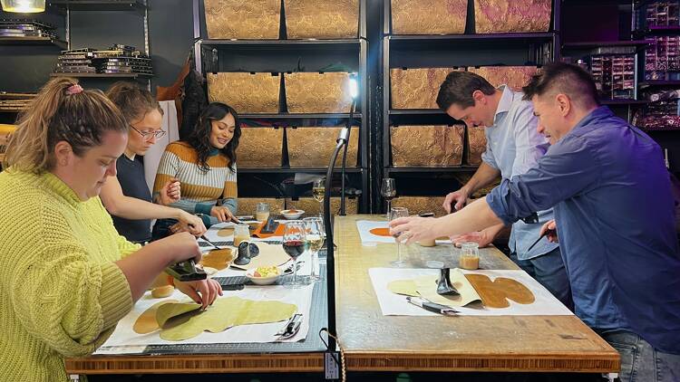 A group of people works on handbags around a table.