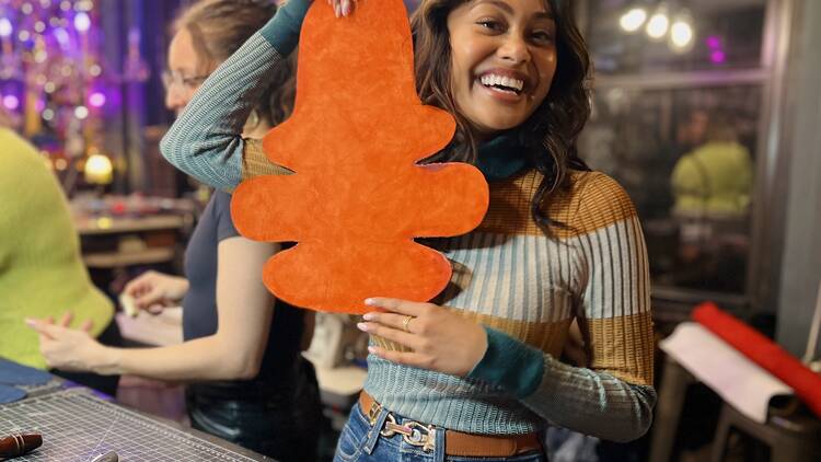A woman holds up an orange piece of leather, which will become a purse.