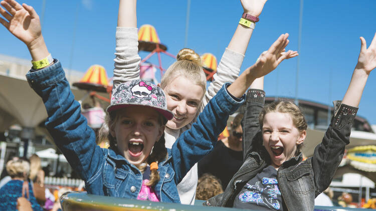 Three girls on a tea cup ride with their hands in the air