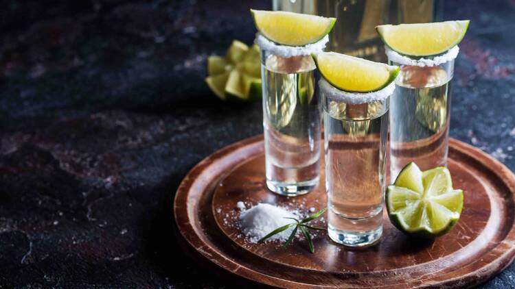 Three shots of tequila with lime wedges