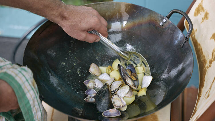 Chef stirring pipis and potato in a pan.
