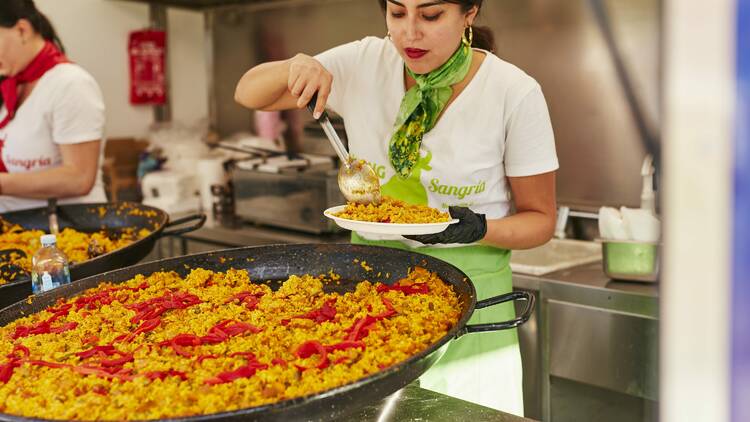 A person serving up from a huge pan of paella. 