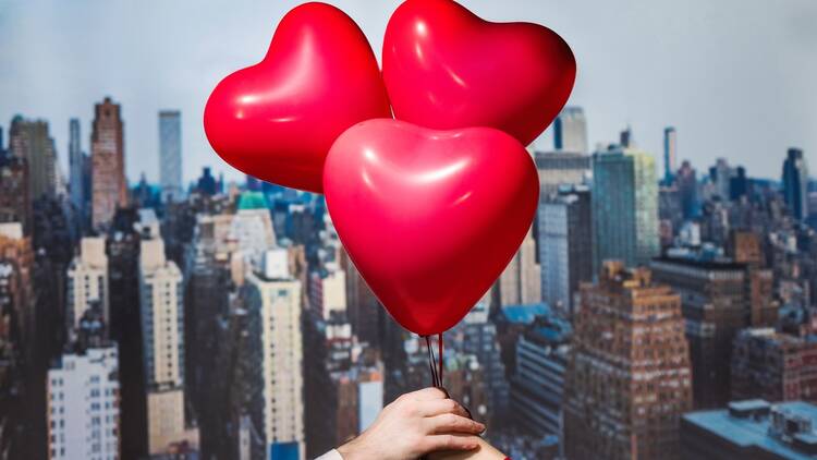 Valentines day in the New York city. man and woman hands holding three red balloons in form of heart over Manhattan and skyscrapers. Сoncept. America. USA. Aerial view.