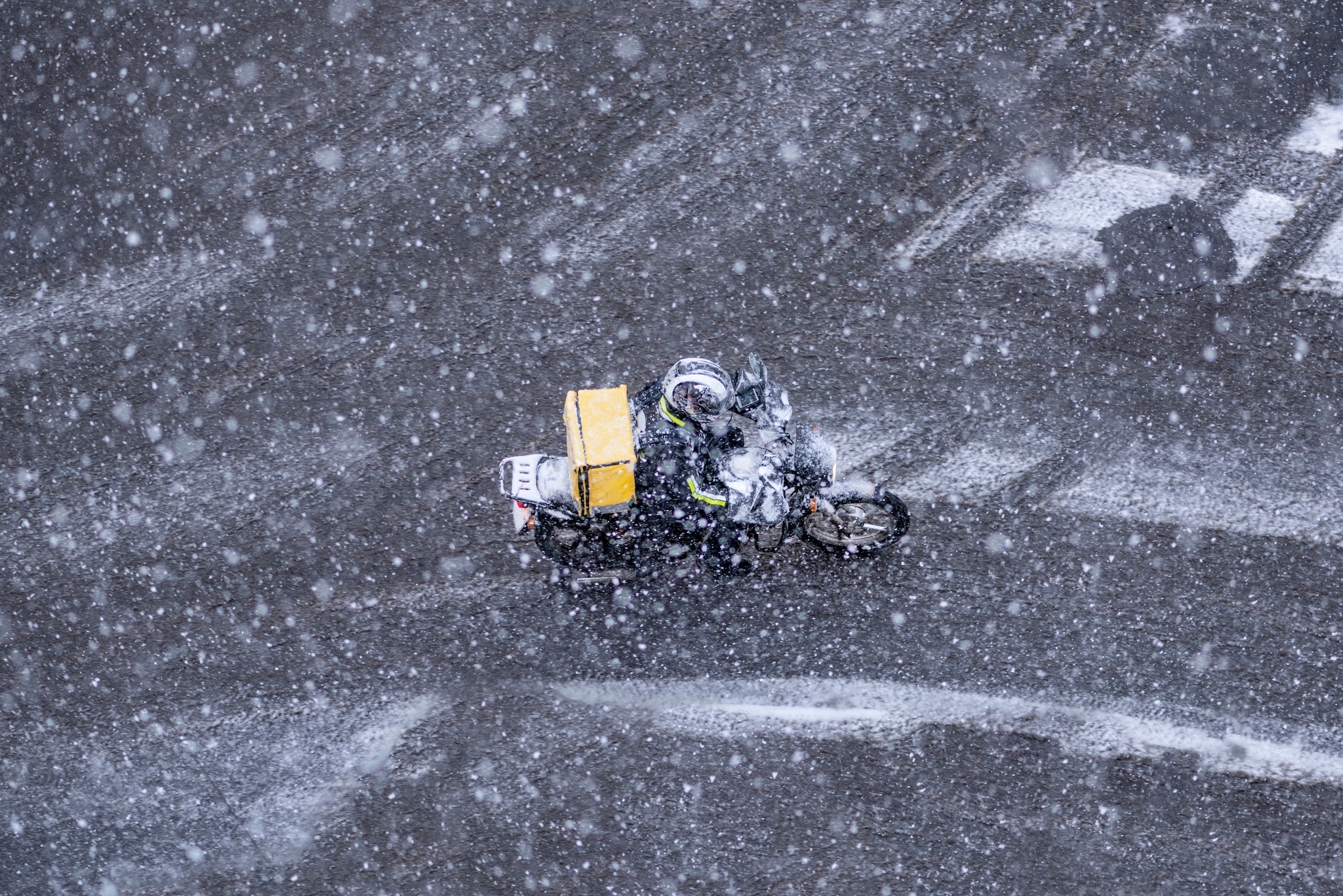 Food delivery courier on a motorcycle rides under the snow with yellow backpack