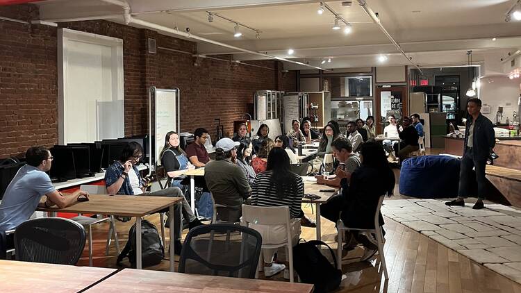 A table of people sitting on desks in a big room