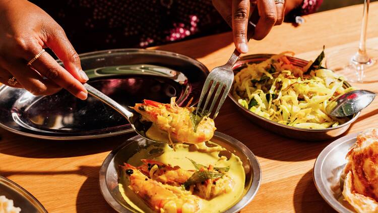 Diner portioning out Toddy Shop's prawn moilee dish with a knife and fork.