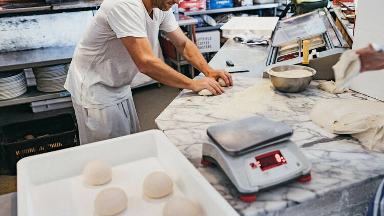 A pizza chef rolling dough