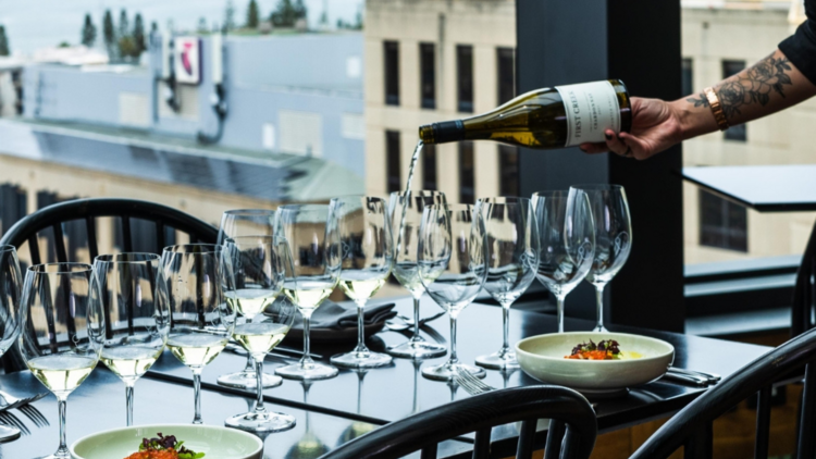 Glasses being filled with white wine at a formal table overlooking coastal views