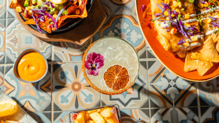 Assorted Mexican dishes and a Margarita on a colourfully tiled table.