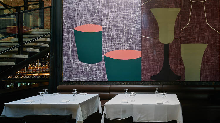 Set tables with white tablecloths in front of an art-decorated wall.