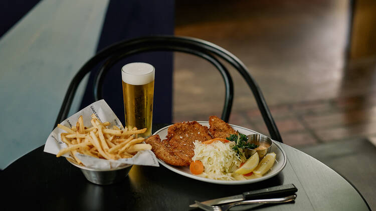 A plate of schnitzel and slaw with a side of chips and a pint of beer.