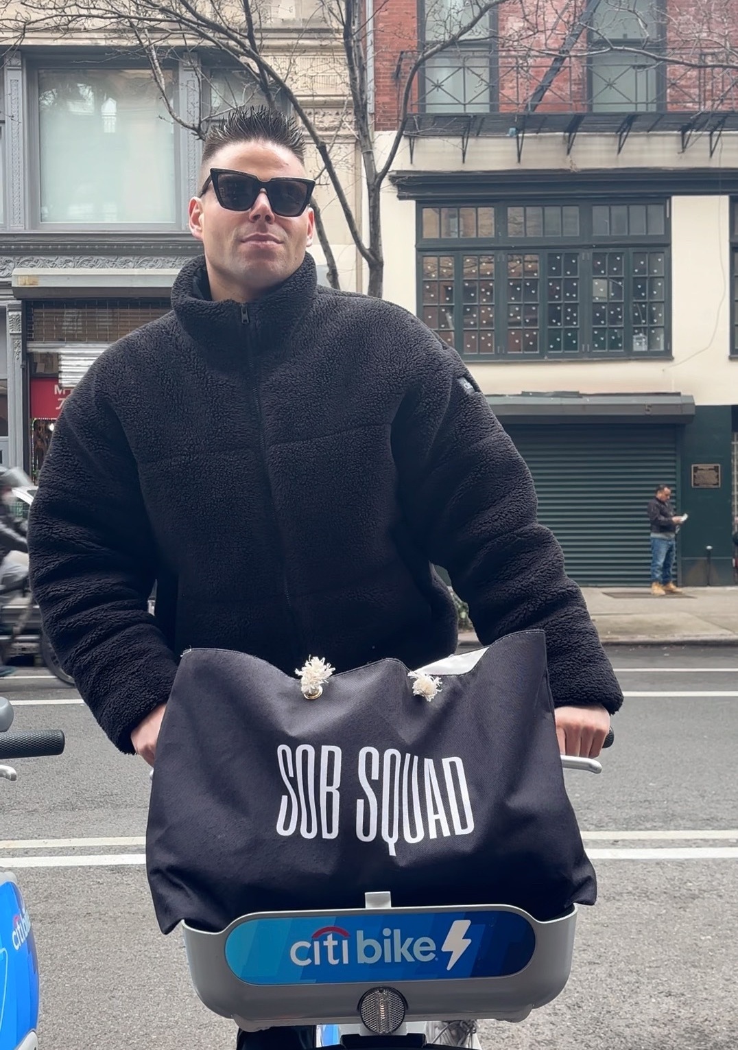 A man on a bike with a bag reading "Sob Squad."